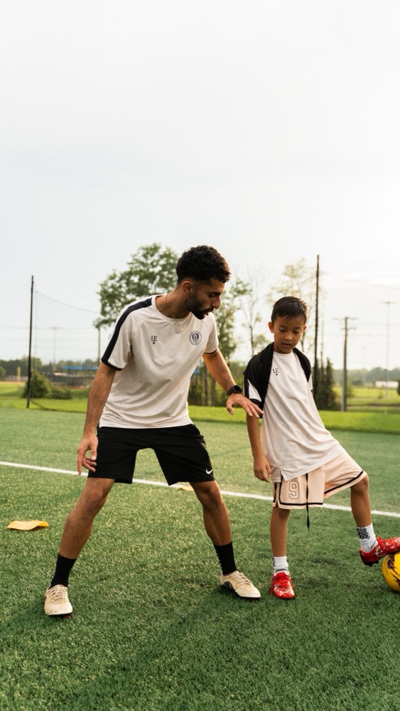 A coach working closely with a player who has his foot on the ball