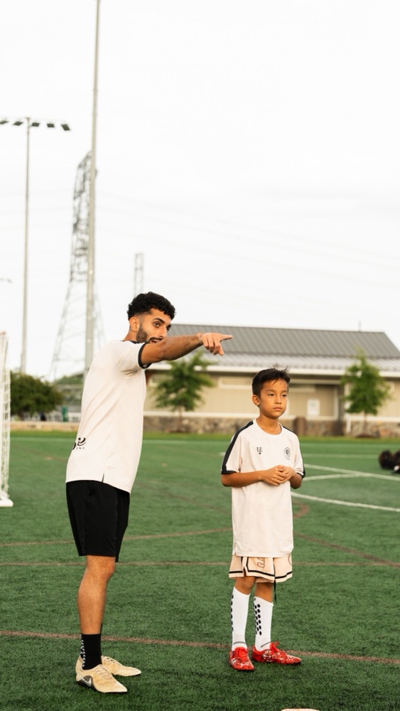 A coach pointing across the field while standing beside a player