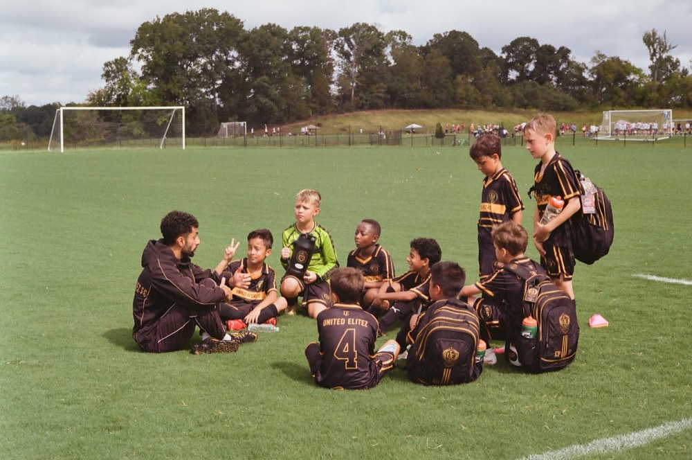 A coach talking with a circle of seated players on the field